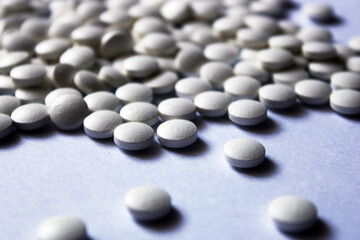 A lot of white pills are scattered on a white background.