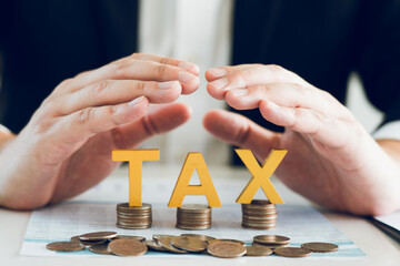 Businessman's hand is protecting letters with the word tax on a coin. Tax concept.