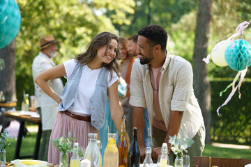 Friends talking, flirting and having fun at summer grill garden party. Multiracial couple hosting garden party.