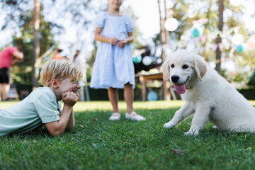 Children playing with a small puppy at family garden party. Portrait of little boy lying on grass...