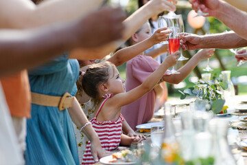 Family clinking glasses at summer garden party, kids clinking with nonalcoholic drink, lemonade. Celebratory toast at table. Big family garden bbq. - 750472270