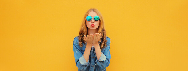 Portrait of beautiful stylish young woman blowing kiss posing on yellow studio background