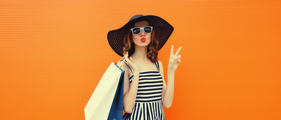 Beautiful happy woman model with shopping bags in summer black hat, dress on orange background