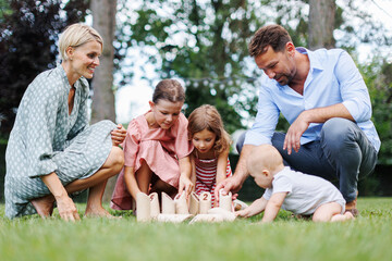Family playing in grass with wooden garden game. Father, mother, and three children having fun at...