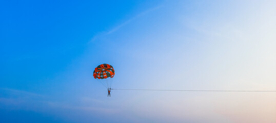 Parasailing extreme sports on beach in blue sky background. Man is parasailing in the blue sky. Paragliding in the clear sky above the sea. - obrazy, fototapety, plakaty