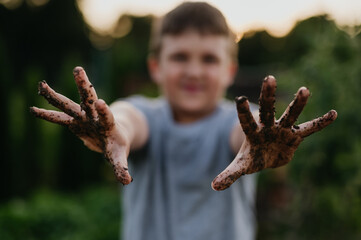 Boy has dirty hands after work in garden. Caring for vegetable garden and growing, planting spring...