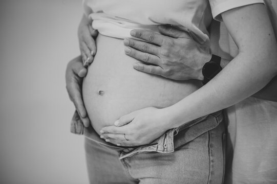 Cropped image of husband holding hands belly of his pregnant wife. Pregnant woman and loving handsome man hugging tummy at home. Loving Couple. Parenthood concept. Baby Shower. Black and white photo