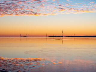 Naklejka premium Colorful sunset by the calm sea with fluffy clouds in the sky and windmills on the horizon, Bothnian Bay, Baltic Sea, Finland