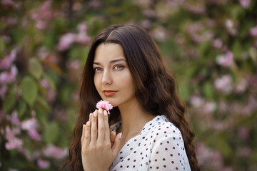 Spring girl face. Close up portrait of tender woman at sakura flowers background. Hanami celebration in sakura blooming garden. Young stylish woman standing in sakura park and enjoy beauty of pink