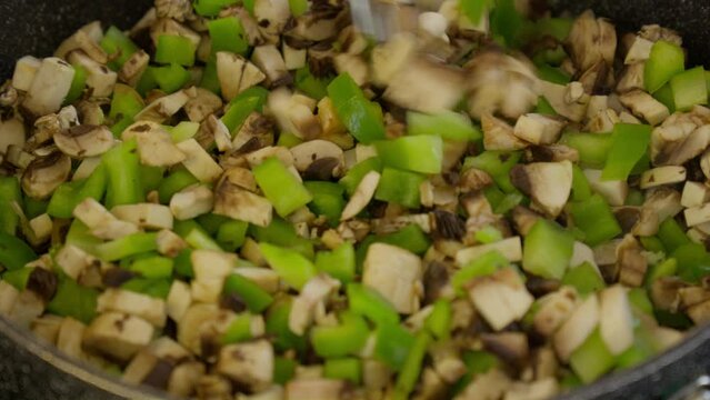 Stri diced veggies mushroom and green bell pepper in frying pan skillet