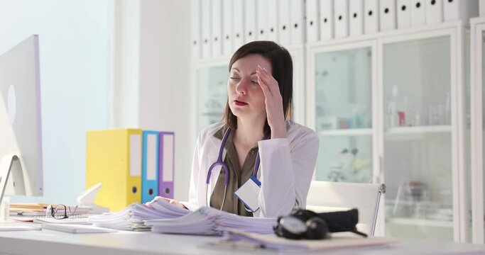 Tired sad woman doctor studying lot of papers documents in clinic 4k movie slow motion. Bureaucracy and paper work in medicine concept