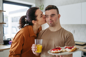 Fototapeta na wymiar Young man with Down syndrome serving breakfast to his mother as a Mother's Day gift. Concept of Mother's Day and maternal love to disabled children.