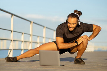 Athlete guy in deep lunge uses laptop for outdoor workout