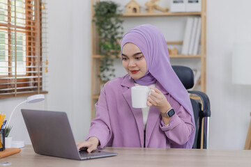 Asian islamic woman using laptop computer at desk in office.