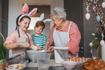 Grandmother with grandchildren preparing traditional easter meals, baking cakes and sweets. Passing...