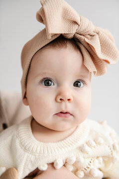 Cute Baby, 6 months old closeup. A beautiful little girl with big eyes and a big bow headband on her head. Portrait of an adorable baby girl with bow in hair isolated in white background.