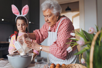 Grandmother with granddaughter preparing traditional easter meals, baking cakes and sweets. Passing down family recipes, custom and stories. - 750490468