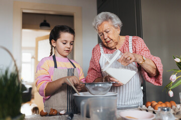 Grandmother with granddaughter preparing traditional easter meals, baking cakes and sweets. Passing down family recipes, custom and stories.