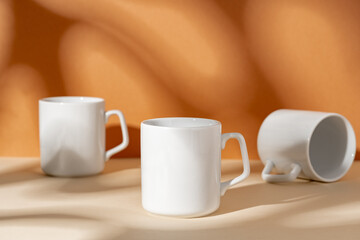 White ceramic mugs on peach background with shadows