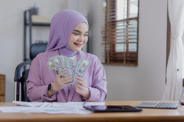 Asian islamic businesswomen holding dollars in hand at office desk.