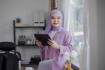 Happy young asian islamic women using digital tablet standing at office desk. 