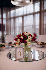 Red and white flower arrangements of tulips in vases, spring flowers. On the festive table in the wedding banquet area, compositions of flowers and greenery, candles are placed.
