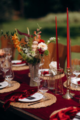 Red flower arrangements in vases, colorful decor, autumn flowers. On the festive table in the wedding banquet area, compositions of flowers and greenery, candles are placed.