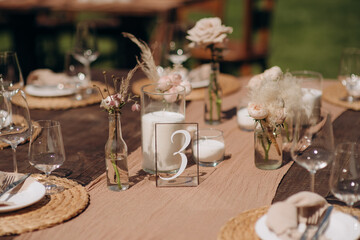 Many small pink and white flower arrangements with roses, eustoma and various flowers in clear glass vases. On the festive table in the wedding banquet area, compositions of flowers and greenery, cand