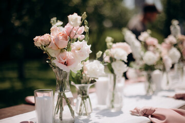 Many small pink and white flower arrangements with roses, eustoma and various flowers in clear glass vases. On the festive table in the wedding banquet area, compositions of flowers and greenery, cand