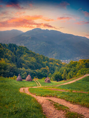 Three haystacks on the side of old dirty road in Carpathian Roztoky village. Majestic summer sunset on Carpathian Mountains, Ukraine, Europe. Beauty of countryside concept background..