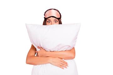 Young gorgeous shocked lady wearing eye mask, hugging pillow, hiding. Isolated over pink pastel...