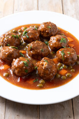 Meatballs, green peas and carrot with tomato sauce on wooden table. Close up