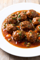 Meatballs, green peas and carrot with tomato sauce on wooden table. Close up
