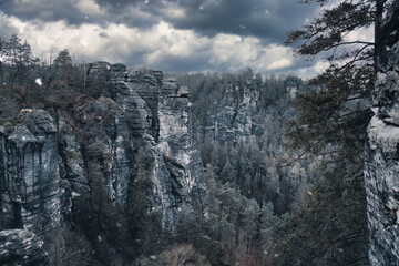 Rugged rocks at Basteibridge during snowfall. Wide view over trees and mountains