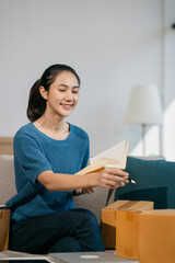 woman start up small business owner writing address on cardboard box at workplace.small business entrepreneur SME or freelance asian woman working with box at home.