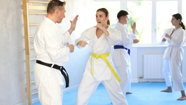 Adult man and young woman karatekas train karate in group in studio