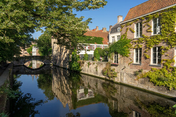 Fototapeta na wymiar Meestrat bridge and historic buildings reflected on the canal in the old town of the beautiful city of Bruges in Belgium in a sunny day.