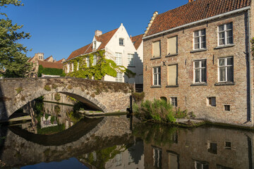 Fototapeta na wymiar Peerden bridge and historic buildings reflected on the canal in the old town of the beautiful city of Brugge in Belgium in a sunny day.