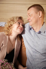 Loving adult couple communicates and embraces privately in the living room or in hotel. The woman is wearing business formal suit and man is wearing jeans and a shirt, indicating a close relationship