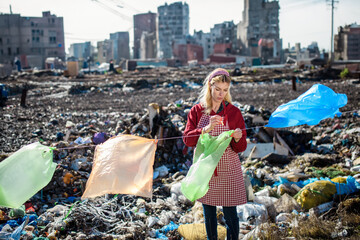 Woman on landfill hanging plastic bags as laundry. Consumerism versus plastic pollution concept.