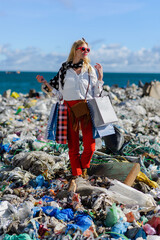 Modern woman on landfill with shopping bags. standing on pile of waste on beach. Consumerism versus...