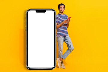 Full size portrait of positive nice man use smart phone large empty space display ad isolated on yellow color background