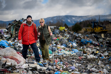 Couple of hikers walking across landfill, large pile of waste, environmental concept and eco...