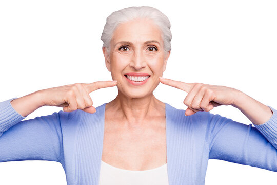 Concept of having strong healthy white perfect teeth at old age. Portrait of old lady with beaming smile pointing on her teeth, isolated over violet background
