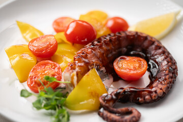 Tentacle squid salad served with tomatoes and lemon on a white plate in a restaurant