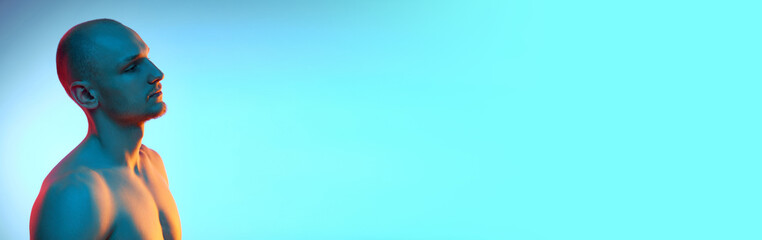 Side view portrait of handsome young bald man posing shirtless on blue background in neon. Concept...