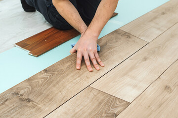 Worker installing new laminated wooden floor. Easy and quick installation of the flooring. Connecting laminate locks.