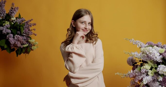 Little fun blonde kid teen teenager girl 13 years in a beige dress she is happy and smiling on a yellow background in the studio. Cheerful teenage girl looking at camera.