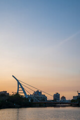Fototapeta na wymiar Sunset over a river with a contemporary suspension bridge silhouette in Tainan, Taiwan