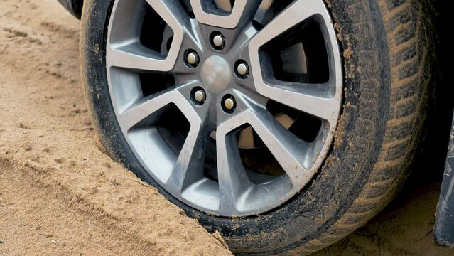 Car big wheels spin and spit up heavy wet sand as unknown driver tries to drive by dirty country road with deep sand drifts. SUV vehicle struggling to gain traction in sand, off road in desert